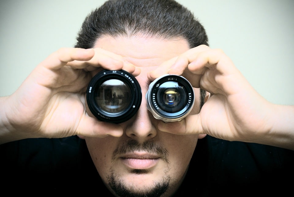 Ein Mann hält zwei Kameralinsen an beide Augen und schaut durch hindurch..